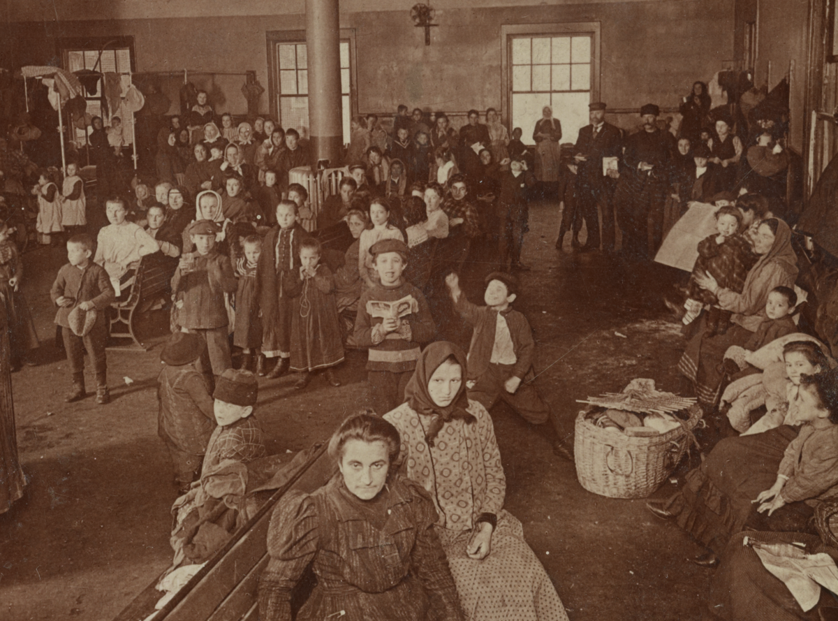 About fifty immigrants waiting for examination and entry into the country. Based on the style of dress and appearance, many are likely from Eastern or Southern Europe.