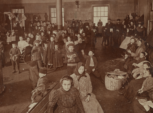 About fifty immigrants waiting for examination and entry into the country. Based on the style of dress and appearance, many are likely from Eastern or Southern Europe.